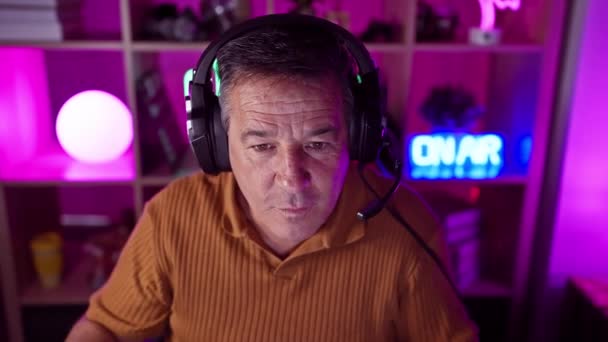Egy Érett Férfi Fülhallgatót Visel Egy Neonfényű Játékteremben Magabiztos Arckifejezéssel — Stock videók