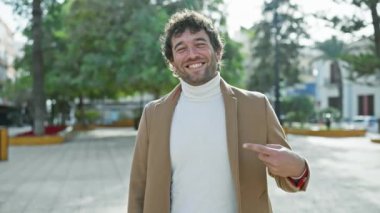 Genç, mutlu İspanyol bir adamın portresi şehir parkında açık havada duran bir palto giyiyor. Neşeli bir adam, umut dolu bir gülümseme, bir jest yoluyla etkili bir fikir gösteriyor.