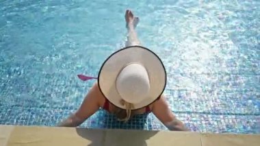 Bir kadın güneşli bir havuzda keyif alır, zarafeti geniş kenarlı bir şapka ve sakin bir suyla vurgulanır..