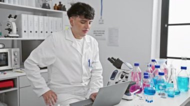 Beyaz önlüklü bir adam mikroskop ve dizüstü bilgisayarla modern bir laboratuvarda sırt ağrısı çekiyor..