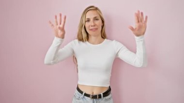 Neşeli genç bir kadın, sarı saçlar, iki eli de dokuz numarayı gösteriyor. Pembemsi arka planda tek başına duruyor, neşeli bir gülümsemeyle..