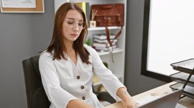 Güzel, genç, esmer bir kız objektife yakalandı. Yüzünde ciddi bir çalışma ifadesi var. Ofis ortamındaki kameraya doğru kendine güvenen bir bakış..