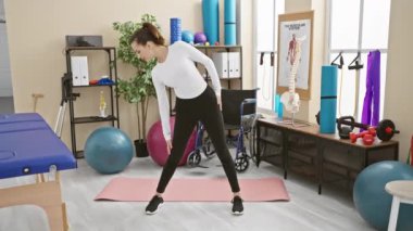 Odaklanmış bir kadın, egzersiz ekipmanları ve rehabilitasyon araçlarıyla çevrili bir fizyoterapi kliniğinde geriliyor..