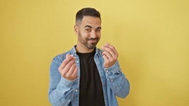 Kot gömlekli, kendine güvenen genç, İspanyol bir adam, kendini para jesti ile gösteriyor, sarı izole edilmiş arka planda maaş için çağrıda bulunuyor.
