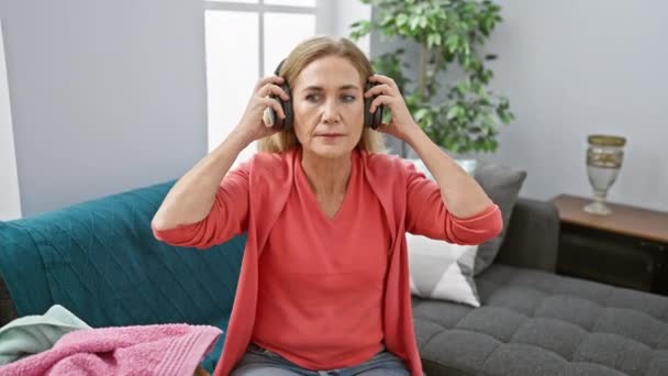 Starší Žena Poslouchá Hudbu Sluchátky Při Skládání Prádla Útulném Obývacím — Stock video