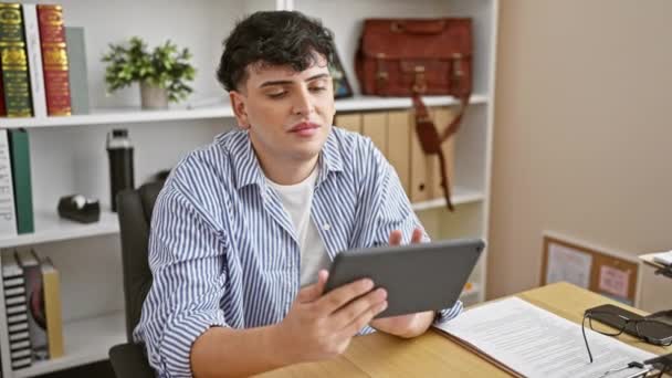 办公室里的一个年轻人 专心致志地使用带有书架和书桌附件的平板电脑 — 图库视频影像