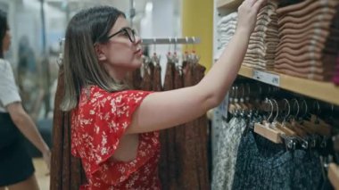 Moda tutkusu! Gözlüklü güzel İspanyol kadın perakende mağazasından şık kıyafetler seçiyor. Alışveriş merkezindeki bir butikten alışveriş yapan esmer bir kızın portresi..