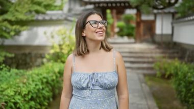 İspanyol kadın, gözlüklü ışıldayan güzellik ve neşe, Kyoto tapınağında neşeli bir ifadeyle etrafa bakıyor, Japon mimarisinin ortasında güvenle duruyor, huzurun tadını çıkarıyor..