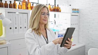 Olgun bir kadın bilim adamı modern bir laboratuvar ortamında bir tableti inceliyor.