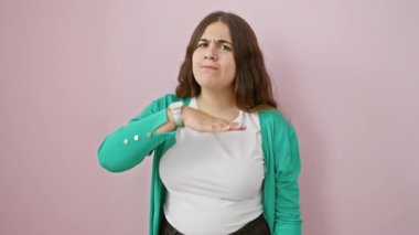 Öfkeli, genç, güzel İspanyol bir kadın, pembe arka planda duruyor, saldırganca bir hareketle boğazını kesiyor, bıçakla tehdit ediyor, öfke ve şiddeti özetliyor..