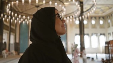 Doha, Katar 'daki Katara Kültür Köyü Camii' nin süslü mimarisinin içinde gözlüklü ve tesettürlü bir kadın.