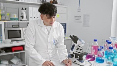 Zevkli genç bilim adamı laboratuvarda başarıdan zevk alıyor. Parlak, dişlek bir gülümsemesi olan kendine güvenen bir adam.