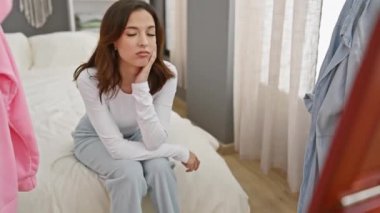 Modern bir yatak odasında beyaz bir yatakta oturan düşünceli genç İspanyol kadın.