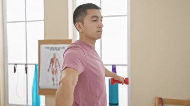 Odaklanmış genç bir adam, parlak bir rehabilitasyon kliniğinde dambıllarla egzersiz yapıyor..