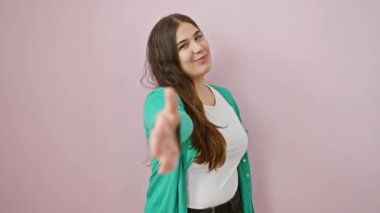 Güzel, başarılı İspanyol kadın gülümsüyor, pembe arka planda dikiliyor, güvenli bir şekilde selamlaşıyor - başarılı bir iş ortaklığının sembolü olarak..