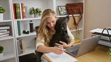 Genç bir kadın modern bir ofiste çalışırken siyah labradoruna sevgiyle sarılıyor ve uyumlu bir hayvan dostu iş yeri sergiliyor..