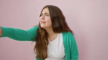 Şaşırmış genç İspanyol kadın, ağzı açık, şaşırmış bir şekilde, izole edilmiş pembe arka planda şaşırtıcı bir şeyi işaret ediyor.