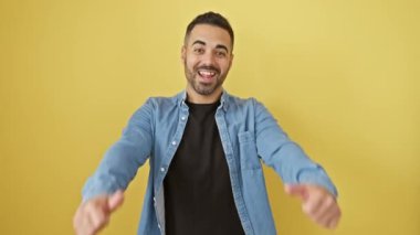 Kot gömlekli neşeli, genç İspanyol adam zaferi sevinçle kutluyor, başparmağını kaldırıyor. Sarı arka planda mükemmel izole edilmiş bir kazanan jesti..