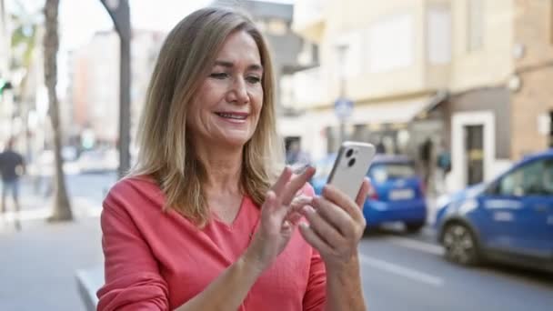 穿着粉色衬衫的金发女士在繁忙的城市街道上使用智能手机 — 图库视频影像