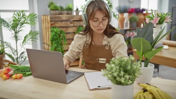 若い女性は植物とチューリップに囲まれた花屋でノートパソコンで働いています — ストック動画