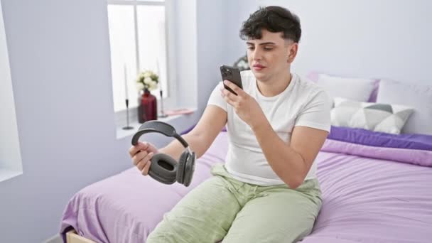 Mladý Muž Zkoumá Smartphone Zatímco Drží Sluchátka Moderní Ložnici — Stock video