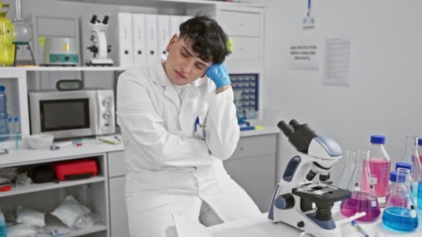 Tired Young Man Lab Coat Rests Amidst Laboratory Equipment Portraying — Stock Video