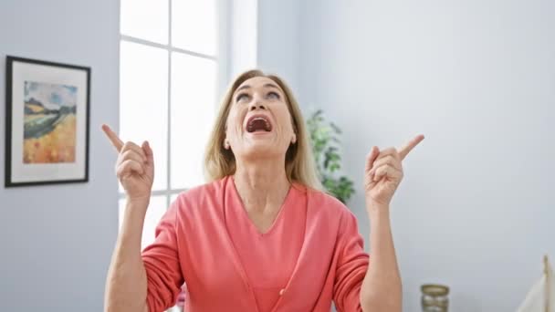 Mujer Rubia Mediana Edad Asombrada Sentada Sofá Casa Señala Shock — Vídeo de stock