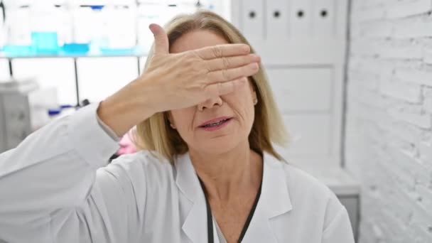 陽気な中年ブロンドの科学者は ラボで手で目を覆う喜びのサプライズを隠しています — ストック動画