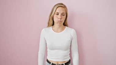 Sinirli genç sarışın kadın, agresif bir ifadeyle çılgınca bağırıyor ve soyutlanmış pembe bir arka planda kollarını kaldırıyor. çılgınca öfke ve stres dışavurumu ayakta duruyor..