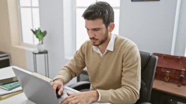 Odaklanmış İspanyol bir adam modern bir ofis masasında dizüstü bilgisayarla çalışıyor, profesyonelliği ve konsantrasyonu gösteriyor..