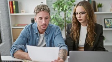 Ofiste, odaklanmış bir erkek ve kadın takım çalışması ve profesyonel işbirliği tasvir eden belgeleri bilgisayarda birlikte incelerler..