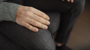 Düşünceli bir adam ellerini sımsıkı tutarak koltuğa oturur. Oturma odasının bulanık zeminine dokunur..