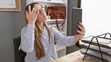 Çizgili tişörtlü kendine güvenen bir kadın modern ofis ortamında akıllı telefonuyla selfie çekiyor..