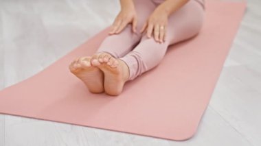 Genç bir kadın evde pembe bir minder üzerinde yoga yapıyor, modern bir oturma odasında vücut bulmuş spor salonu ve sükunet..