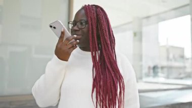 Saçları örgülü Afrikalı Amerikalı bir kadın şehrin dışında akıllı telefondan konuşuyor..
