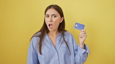 Genç, güzel İspanyol kadın, öfkeden köpürüyor, öfkeden köpürüyor. Bir kredi kartı tutuyor, öfkeli bir çığlık atıyor, sarı bir arka planda izole edilmiş.