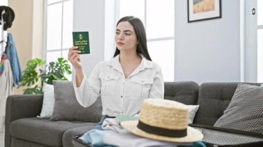 Neşeli, genç, İspanyol bir kadın, Suudi Arabistan pasaportuyla evde oturuyor, tek parmağıyla güvenle işaret ediyor, heyecan verici bir fikre ya da parlak yüzüne soru işareti yapıyor.