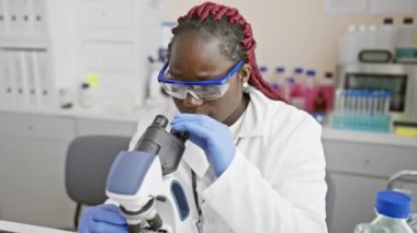 Laboratuvar ortamında mikroskop kullanan Afrikalı kadın bilim adamı araştırma ve sağlık konseptini resmediyor
