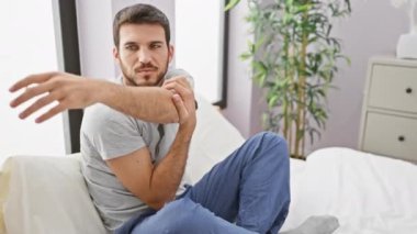 Evdeki yatak odasında kollarını uzatan sakallı genç bir İspanyol sabah rutinini ve rahatlama duygusunu aktarıyor.