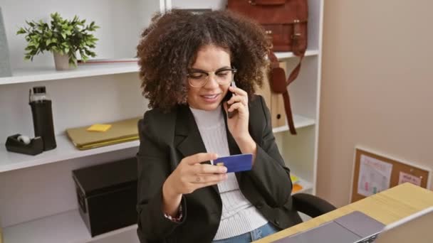カーリーヘアの若いヒスパニック女性 オフィスでクレジットカードを持っている電話で話す — ストック動画