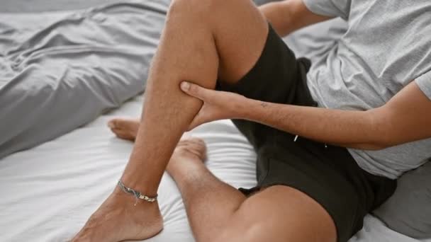 Мужчина Браслетом Сидит Кровати Удобной Спальне Демонстрируя Голые Ноги Расслабленную — стоковое видео