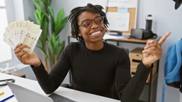 オフィスのドレッドロックを持つヨーヨーの若い黒人女性は 誇らしげにデンマークのクローネ紙幣をブランドしています 笑顔と自信に満ちたジェスチャーで 彼女は片側を指差し — ストック動画