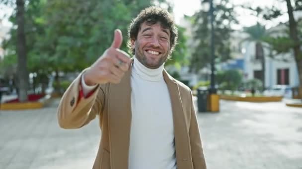 陽気な若いヒスパニックの男性は 公園に立って 優れた承認サインを点滅し 陽性と喜びの笑顔で成功を体現しています — ストック動画