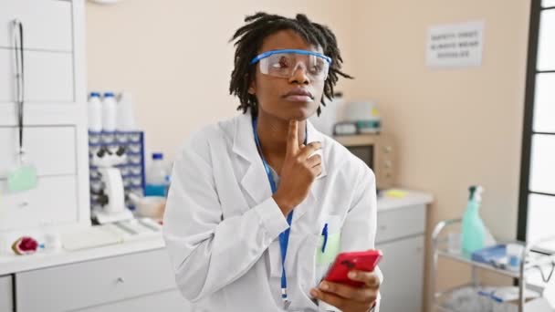 驚いた若い黒人女性は 実験室でスマートフォンで作業するドレッドロック 幸せな顔で指を指し ナンバーワンのアイデアはスマートな質問をスパークします — ストック動画