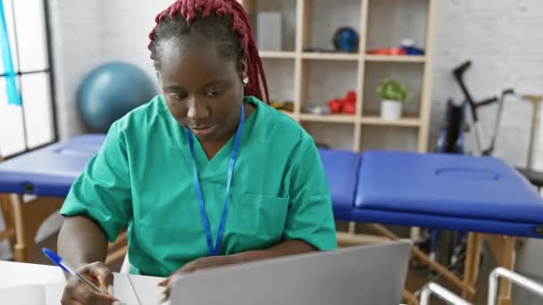 Сфокусированная Женщина Косичками Работающая Ноутбуком Физиотерапевтической Клинике Одетая Зеленый Скраб — стоковое видео