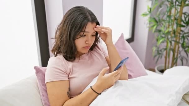 彼女の寝室で懸念されるヒスパニック系女性は 接続性とプライバシーの問題を象徴するスマートフォンに注意深くメッセージを読みます — ストック動画