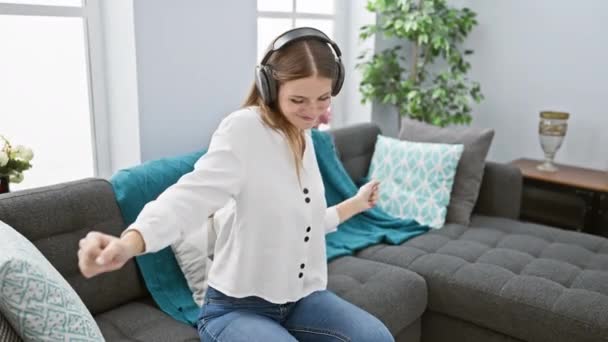 Radosna Młoda Kobieta Słucha Muzyki Słuchawkami Przytulnym Salonie Wyrażając Szczęście — Wideo stockowe