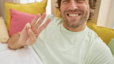 Neşeli, genç, beyaz bir adam, gururla üç parmağını gösteriyor. Hepsi de rahat yatak odası pijamalarıyla ışıldıyor.