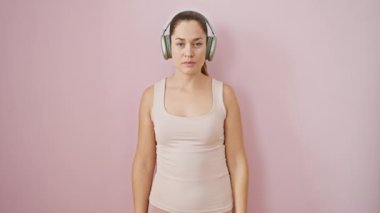 Spor kıyafetleri içinde gülümseyen genç bir kadın, pembe izole edilmiş arka planda kulaklıklar. Serin, kendine güvenen mavi gözlü, mükemmel, mutlu bir gülümseme, dişler ve her şey..