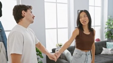 Mutlu ırklar arası bir çift, bir erkek ve bir kadın, samimi, modern bir oturma odasında kucaklaşıyorlar, sevgiyi ve birlikteliği ifade ediyorlar..